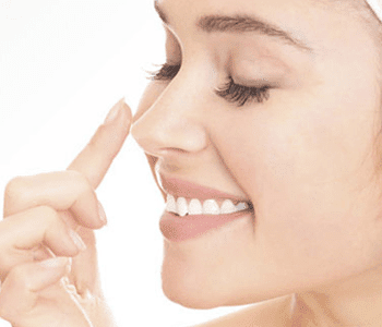 A woman pointing on her nose while smiling. nose-reshaping