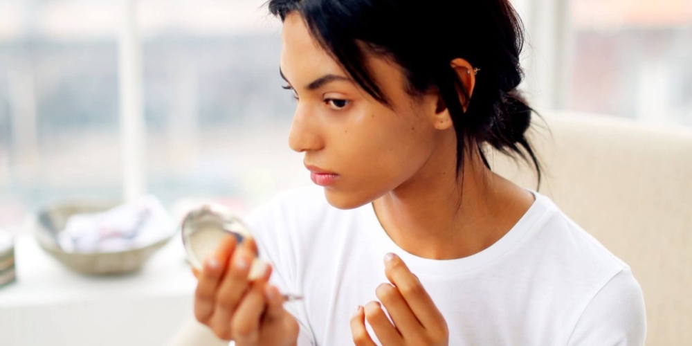 a young woman looks in the pocket mirror sitting on the cream armchair