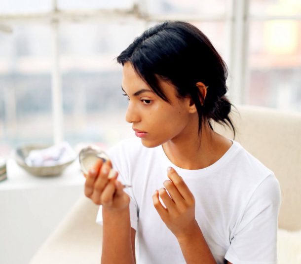 a young woman looks in the pocket mirror sitting on the cream armchair