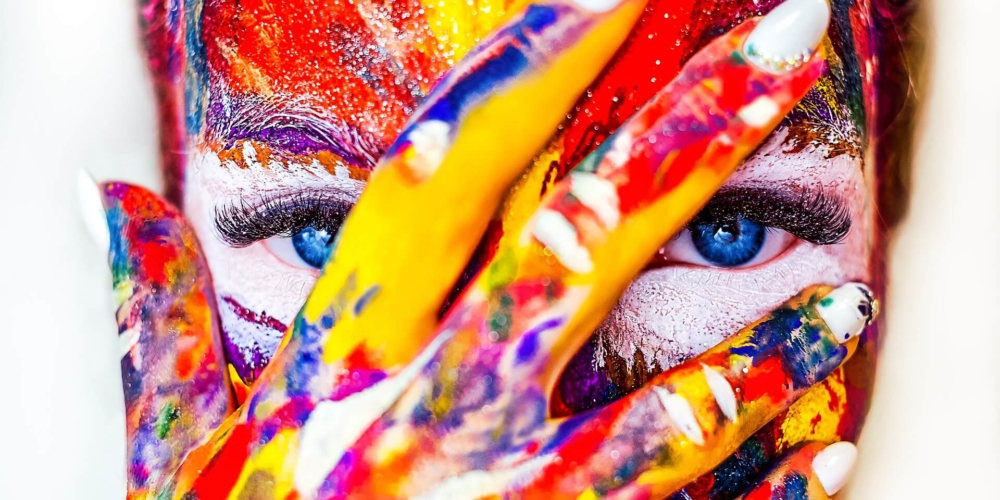 Woman face painted in multi colours, her eyes are ice blue