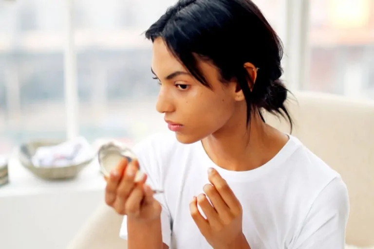 a young woman looks in the pocket mirror sitting on the cream armchair