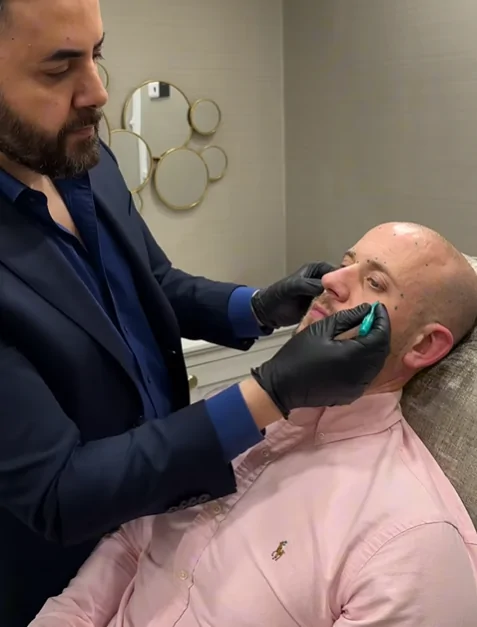 Practitioner administering dermal fillers to a male patient to enhance facial contours and restore volume.
